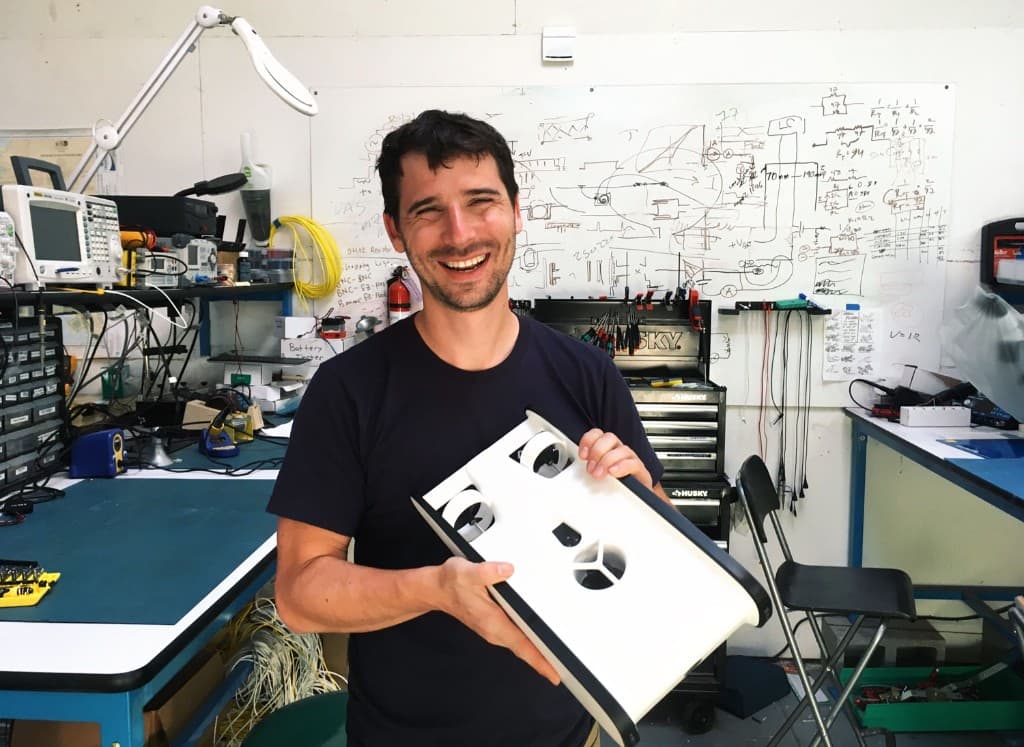 Eric Stackpole smiling in a workshop while holding a prototype.